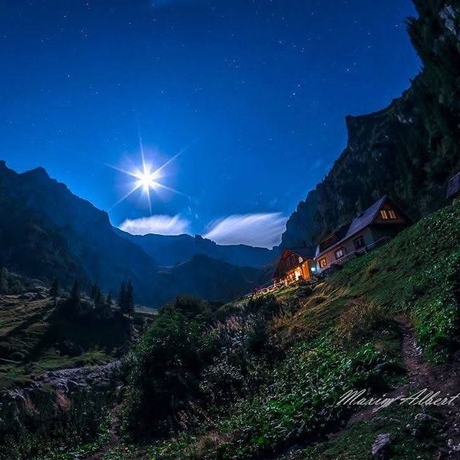 Cabana Mălăiești luminată noaptea, sub lună și cerul înstelat